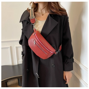 Detail of red lychee grain leather crossbody bag with striped strap on a black trench coat