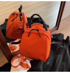 Detail van een feloranje mini-rugzak met een geweven koordhandvat en een metalen D-ring