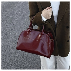 Detail of burgundy tote bag with white contrast stitching and gold metal buckle accents