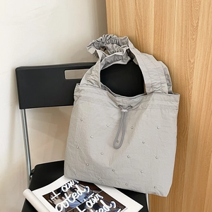 Detail of silver rivets and cloud-pleated handle on a light gray nylon tote bag