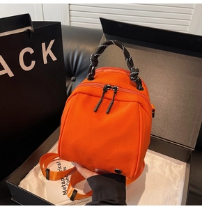 Detail van een levendige oranje mini-tas met geweven touwhandvat in een zwarte geschenkdoos