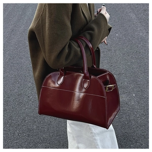 Detail view of dark red leather tote bag with white contrast stitching and gold metal buckle