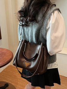 Sac seau rétro en cuir marron avec triangle métallique porté par un mannequin à l'épaule