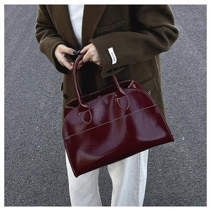 Detail of burgundy glossy leather tote bag with white contrast stitching on street background