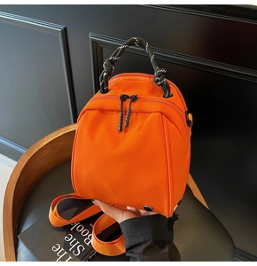 Detail van oranje nylon mini-rugzak met geweven touwhandvat op een leren stoel
