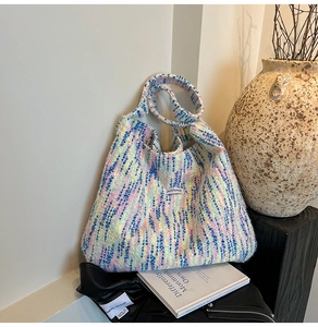 Nahaufnahme einer bunten Tweed-Tragetasche mit weißem Markenlabel in einem Kunst-Ambiente