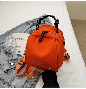 Detailopname van een oranje mini-rugzak met dubbele ritssluiting en geweven handvat
