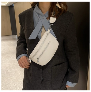 Close-up of white pebble leather sling bag with dual silver zippers and wide strap