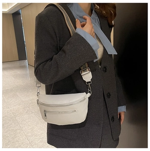 Close-up of white pebble leather sling bag with a vintage patterned woven strap worn by model