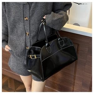 Detailed view of black patent leather tote with contrast white stitching and gold buckles
