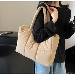 Detailed side view of beige quilted puffer tote bag worn on shoulder by a model