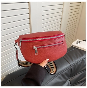 Detail of red pebbled leather saddle bag featuring dual zippers and striped canvas strap