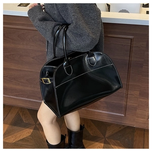 Detail of black tote bag with white contrast stitching and gold metal buckle accents