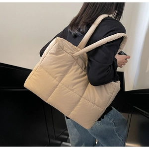 Detail of beige quilted tote bag showing large square stitching and padded shoulder strap