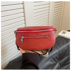 Detail of red pebbled leather saddle bag with silver zippers and striped fabric strap
