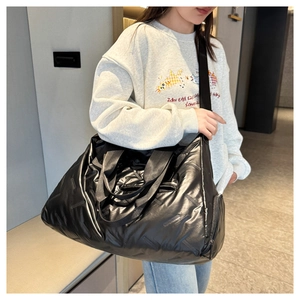Model wearing a large black quilted nylon gym bag with a glossy finish and wide strap
