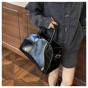 Detail of high-gloss black patent leather tote bag with metal buckles and dual handles