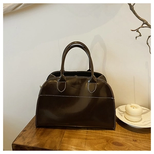 Detail of dark brown glossy leather tote bag featuring white contrast stitching and handles