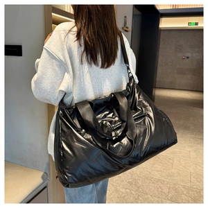 Detail of a shiny black quilted sports bag worn as a crossbody for gym or travel