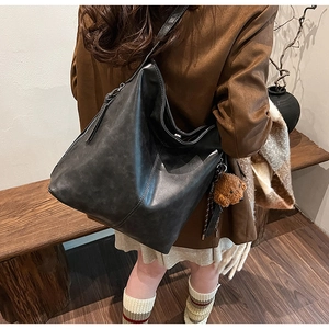 Détail d'un sac seau en cuir noir avec un charmant pendentif ours brun sur la bandoulière