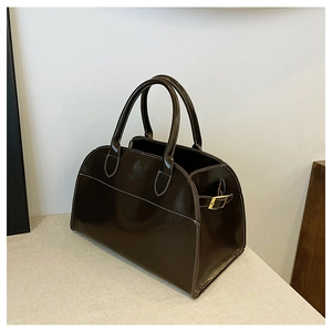 Close-up of brown glossy Boston bag featuring white contrast stitching and gold buckles