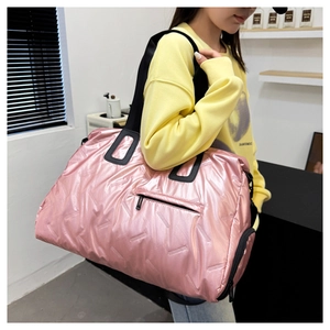 Side view of large pink quilted travel bag with black straps worn by a model