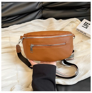 Detailed shot of brown lychee grain leather saddle bag with striped woven strap and silver zippers