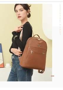 Detail of brown faux leather backpack featuring golden zippers and triangle metal emblem
