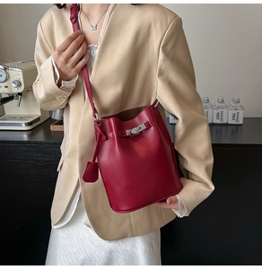 Close-up of a burgundy leather bucket bag with a metal twist lock on a beige outfit