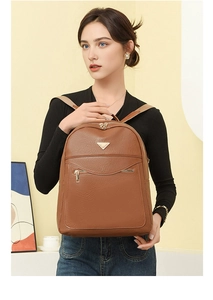 Close-up of brown textured leather backpack with gold triangle detail and zip pocket