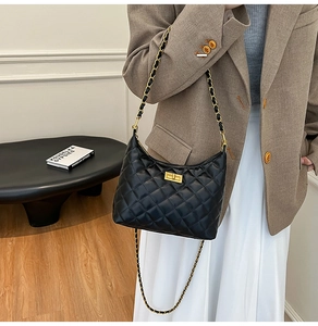 Détail d'un sac bandoulière matelassé noir avec chaîne dorée sur un fond au style minimaliste