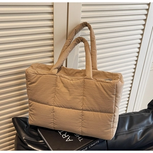 Detail of khaki quilted tote bag with puffer design and matte nylon texture on artsy books