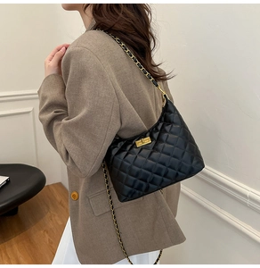 Détail du sac bandoulière noir matelassé avec chaîne dorée porté par un mannequin
