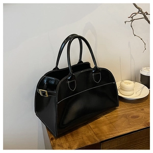 Detail of black glossy tote bag with white contrast stitching and gold hardware on wood