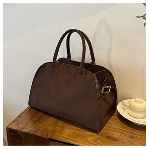 Close-up of matte dark brown tote bag with gold buckle detail on a wooden surface
