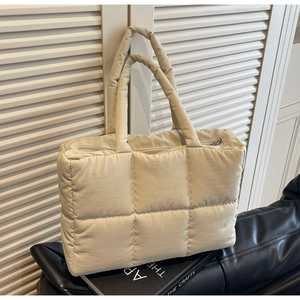 Detailed view of beige quilted puffer tote bag with large square stitching on a leather sofa