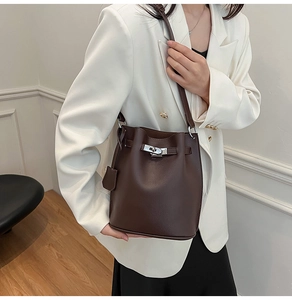 Close-up of brown litchi pattern leather bucket bag with silver twist lock on model