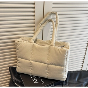Detail of beige quilted tote bag showing padded fabric texture and zipper closure
