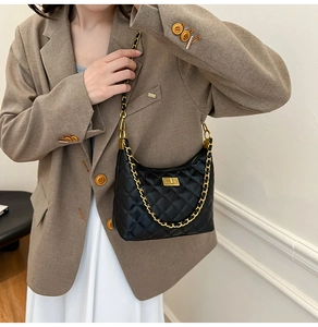 Gros plan d'un sac à bandoulière noir matelassé avec chaîne dorée porté par un mannequin