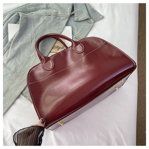 Detail view of burgundy tote bag featuring white contrast stitching and gold metal feet