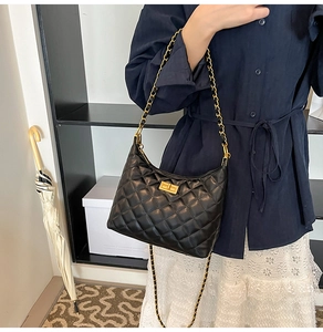 Détail du sac dumpling noir matelassé avec chaîne dorée porté par un mannequin