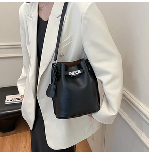 Detail of black pebbled leather bucket bag with silver metal buckle on white blazer