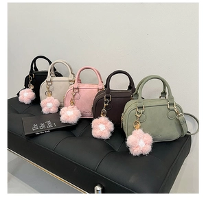 Detail of five mini crossbody bags with suede texture and floral charms on a black bench