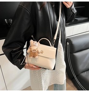 Detail of a creamy white leather square bag with a gold clasp and teddy bear charm