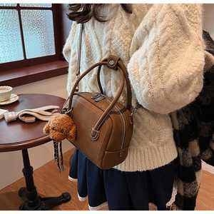 Détail d'un sac à main marron en cuir grainé avec surpiqûres et breloque petit chien