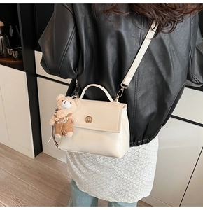 Detail of cream patent leather handbag with gold twist lock and cute teddy bear charm