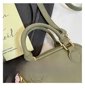 Detail view of grass green suede pillow bag with gold hardware and pink floral charm
