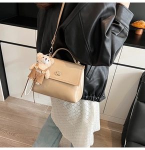 Detail of light beige patent leather bag with gold twist lock and plush bear pendant