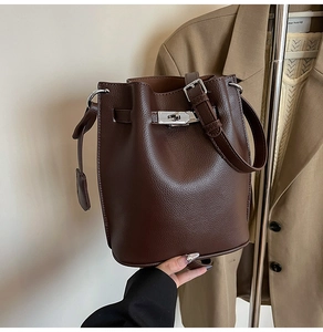 Detail of dark brown lychee grain leather bucket bag with silver lock closure and strap