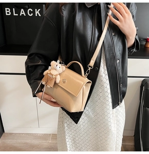 Detail of beige faux leather handbag with metal lock and cute teddy bear charm